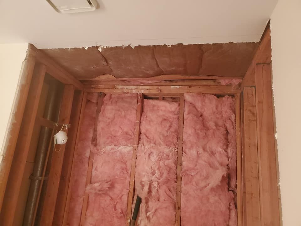 Interior wall studs with pink fiberglass insulation batts installed between them, viewed from below near a ceiling.