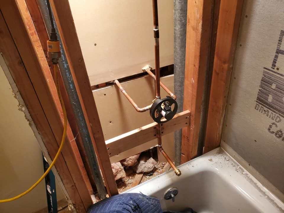 A shower valve and copper plumbing pipes are installed inside an open wall frame above a white bathtub.