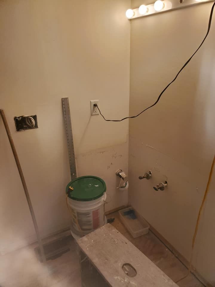 A bathroom undergoing renovation featuring an exposed wall with plumbing pipes, an electrical outlet, and tools.
