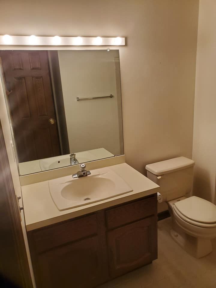 A bathroom vanity with a sink, faucet, and mirror above, next to a white toilet in a room with light beige walls.