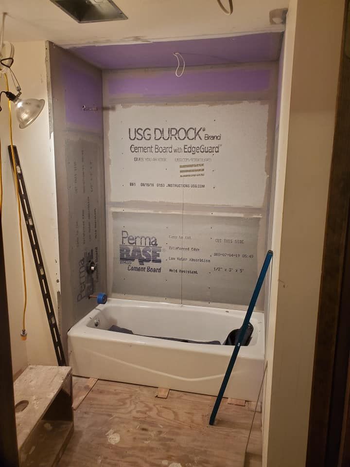 An unfinished bathroom alcove featuring a white bathtub surrounded by gray cement board panels on the walls.