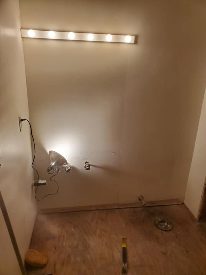 A sparsely furnished room under construction with a long vanity light mounted on the wall and a floor drain.