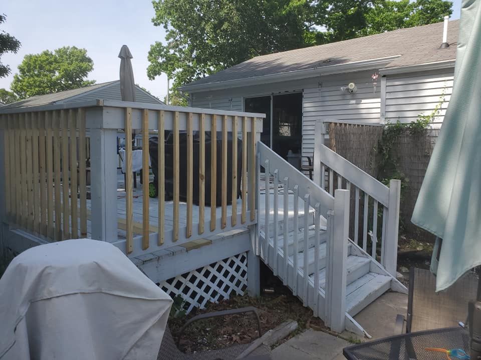 A gray wooden deck with white railings and stairs leads to a house exterior, with a covered grill in the foreground.