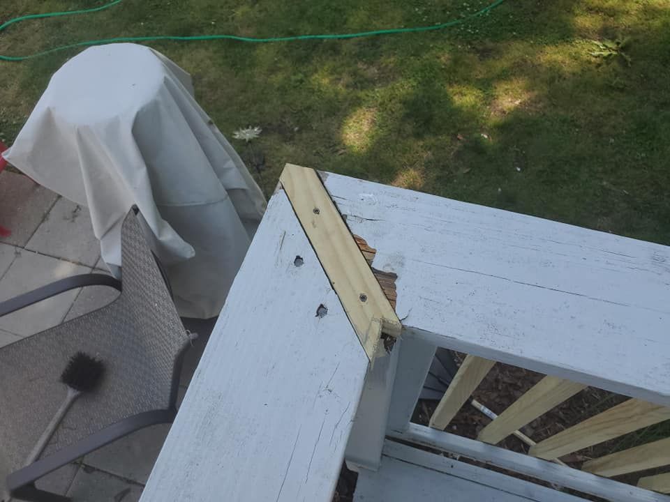 A close-up view of a white deck railing corner showing a mitered joint repair with new wood and visible screws.