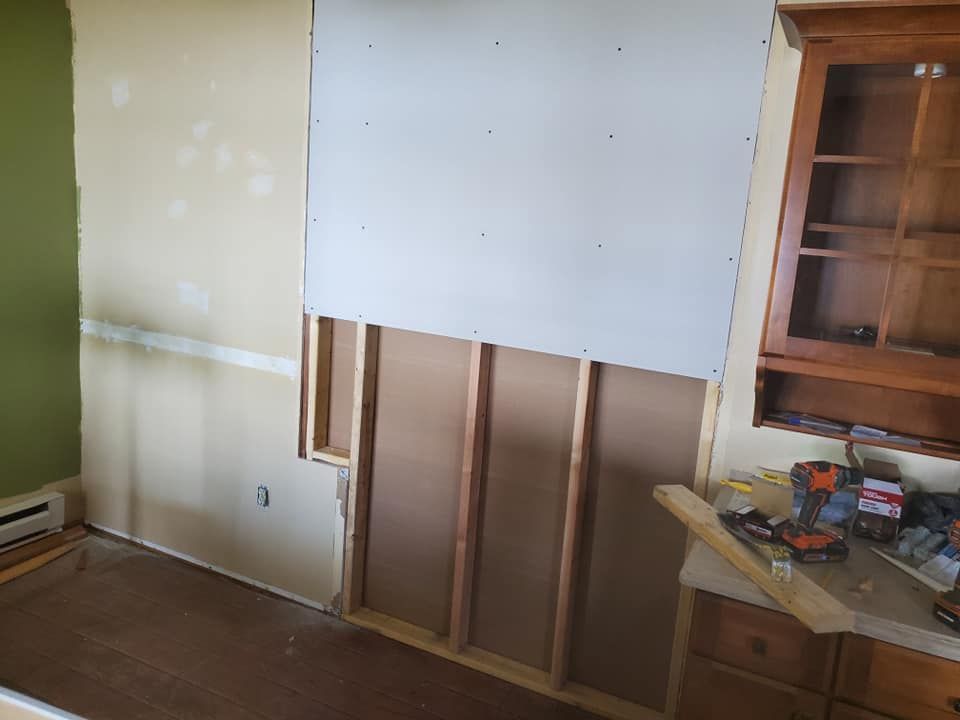 A room interior featuring a wall partially covered in new drywall panels over exposed wooden wall studs.