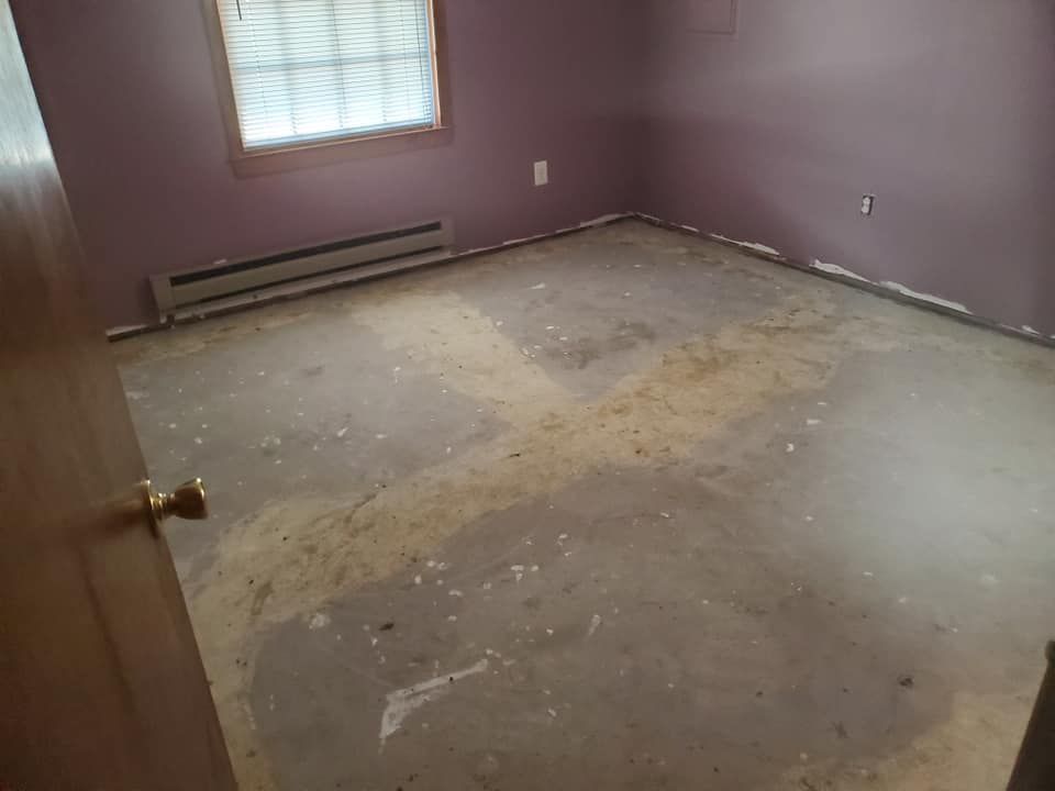 An empty room with dusty purple walls, a window, a baseboard heater, and a bare concrete subfloor.