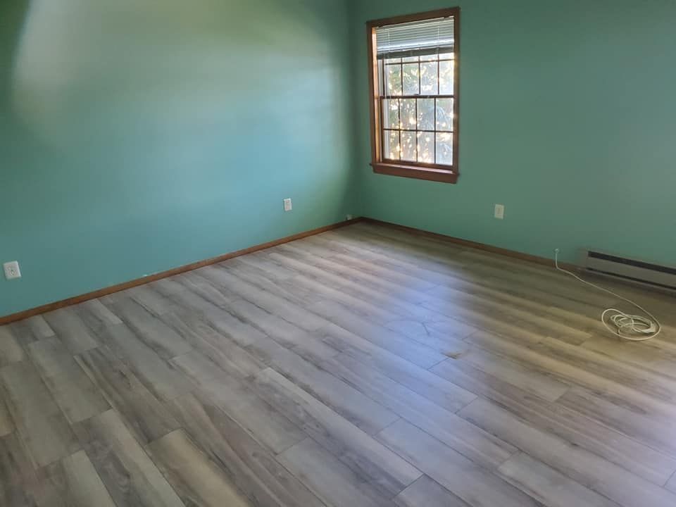 An empty room with light wood-look flooring, teal walls, a single window, and baseboard heating.
