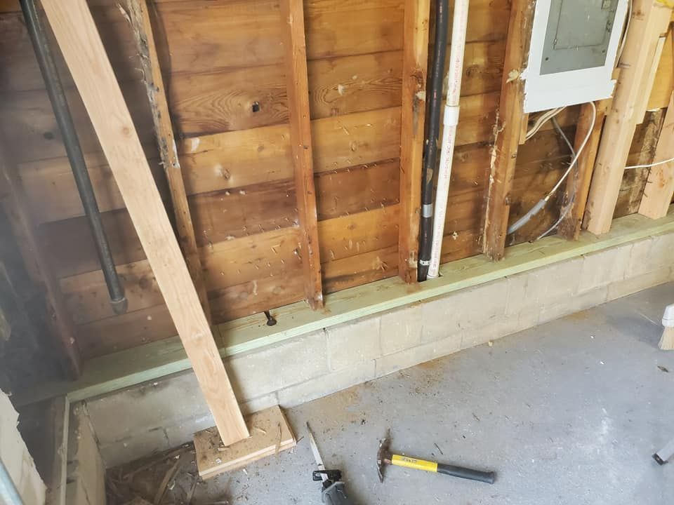 Interior view of a garage wall under construction, showing bare wood studs on a concrete block foundation with tools below.