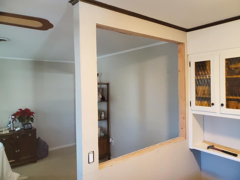 An indoor renovation showing a large rectangular opening cut into a wall between two rooms, with exposed wood framing.