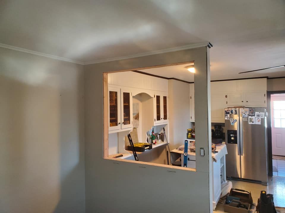 A partially opened interior wall revealing a white kitchen with cabinets, a stainless steel refrigerator, and tools.