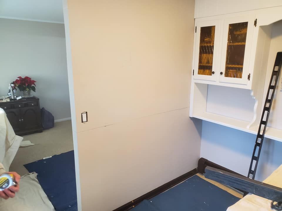 An indoor renovation scene shows a wall being prepped for cabinets, with a white wall-mounted hutch and a level leaning.