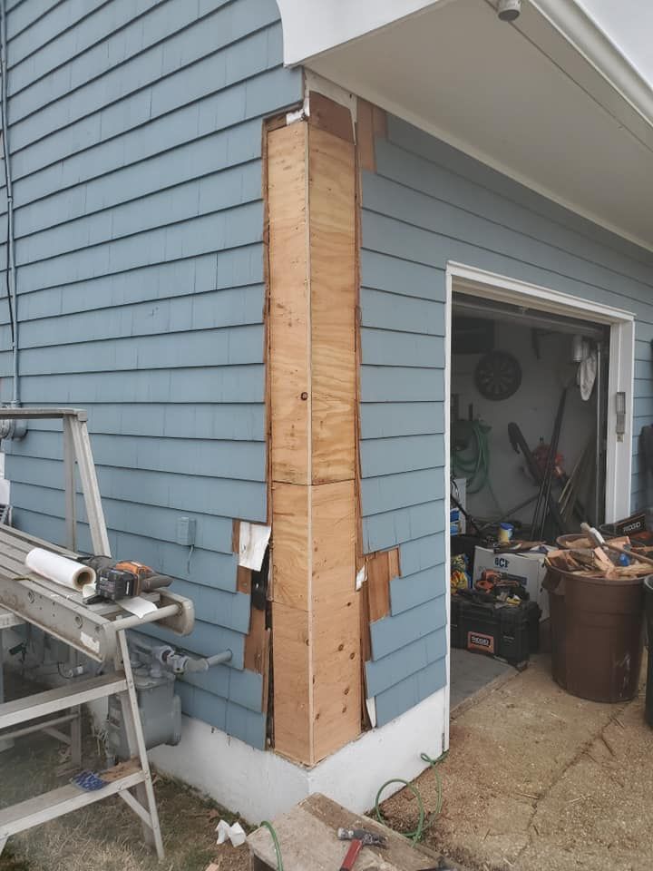 A house corner under construction with exposed plywood sheathing on the exterior wall near an open garage door.