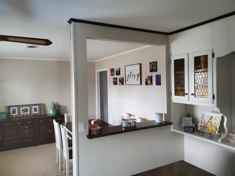 A pass-through kitchen wall with a dark wood counter, open to a dining area with a gallery wall and white chairs.