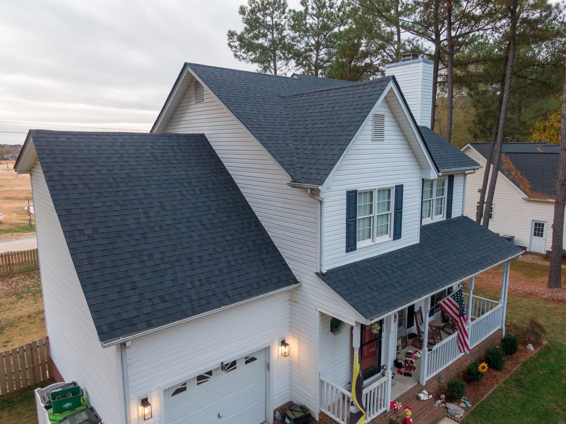 An elevated view of a white two-story house with dark shingles, a front porch, and a garage on a residential lot.