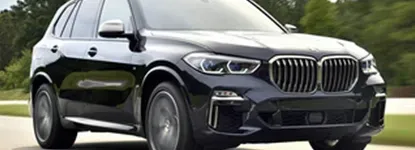 Black BMW X5 SUV driving on a road with blurred background of trees and grass.