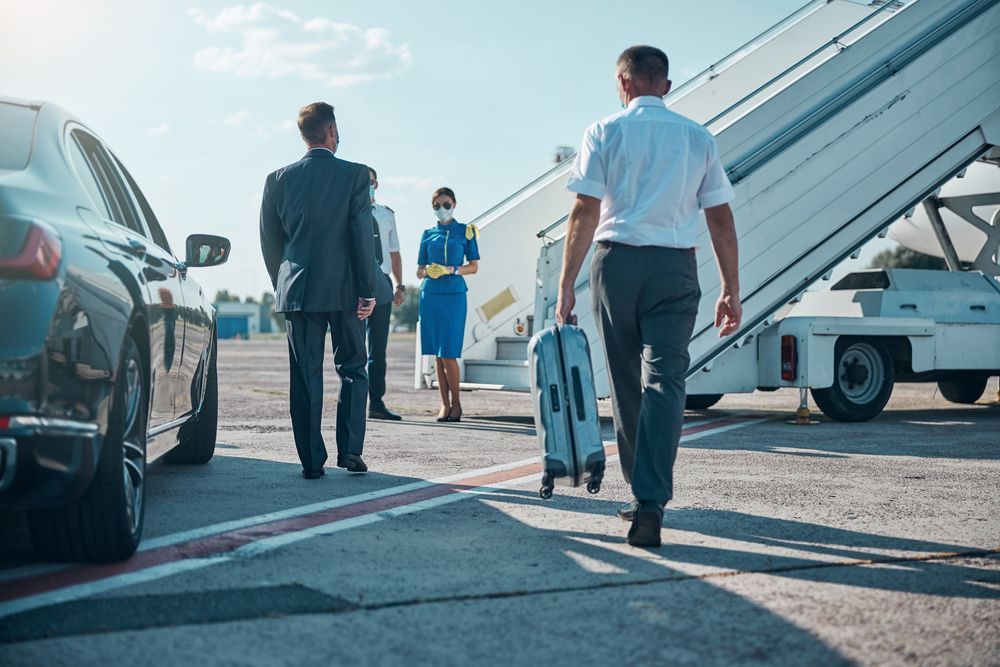 People walking towards a plane, one with a suitcase. Airport tarmac, sunny day.