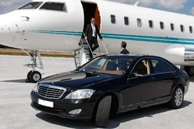 Man exiting private jet, entering waiting black car on tarmac.