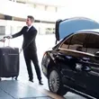 Man in suit loading luggage into a black car's trunk.
