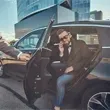 Man in suit exiting a black car, being assisted by someone in a suit near a modern building.
