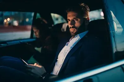 Man in suit looks at phone in car at night.
