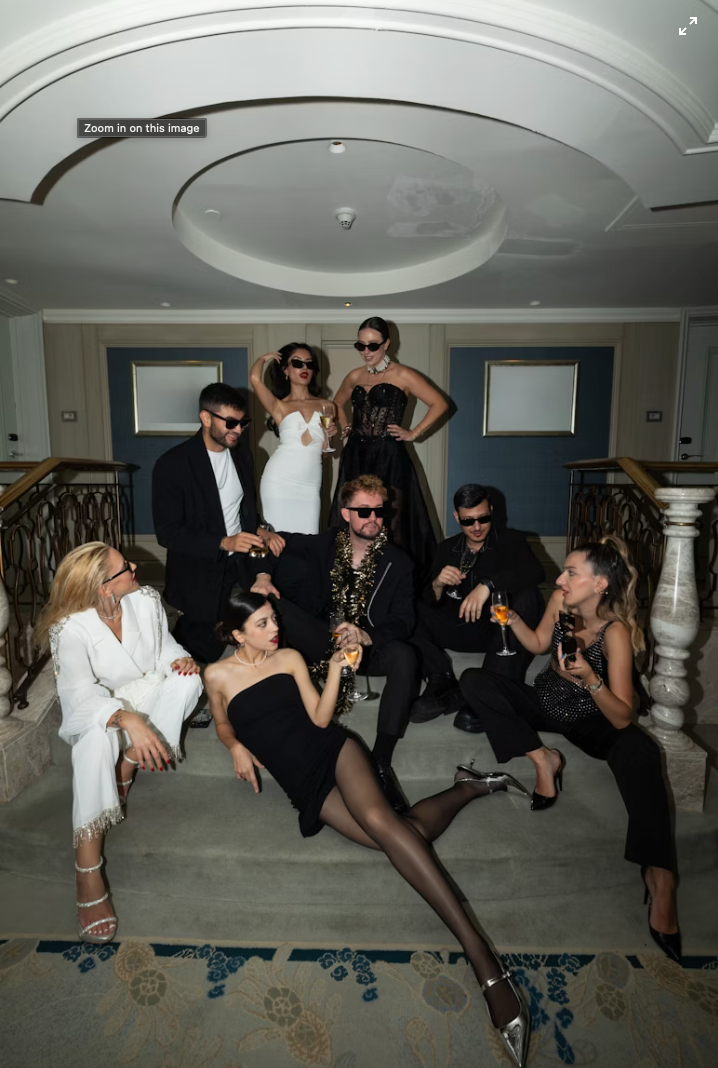 Group of people in formal attire posing on stairs, wearing sunglasses, indoors.