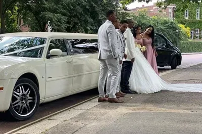 Wedding party next to a white limo; bride in white dress, groomsmen in suits, bridesmaids in pink.