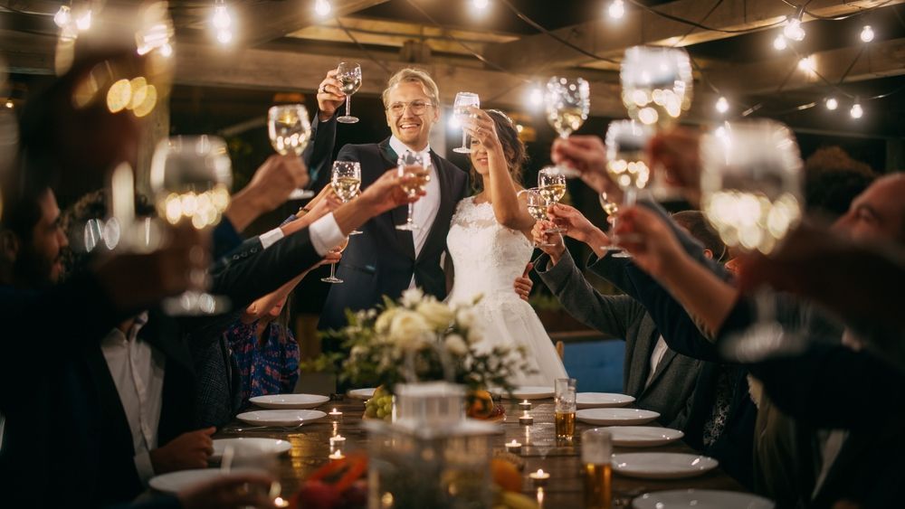 Newlyweds toast with guests at outdoor wedding reception, evening.