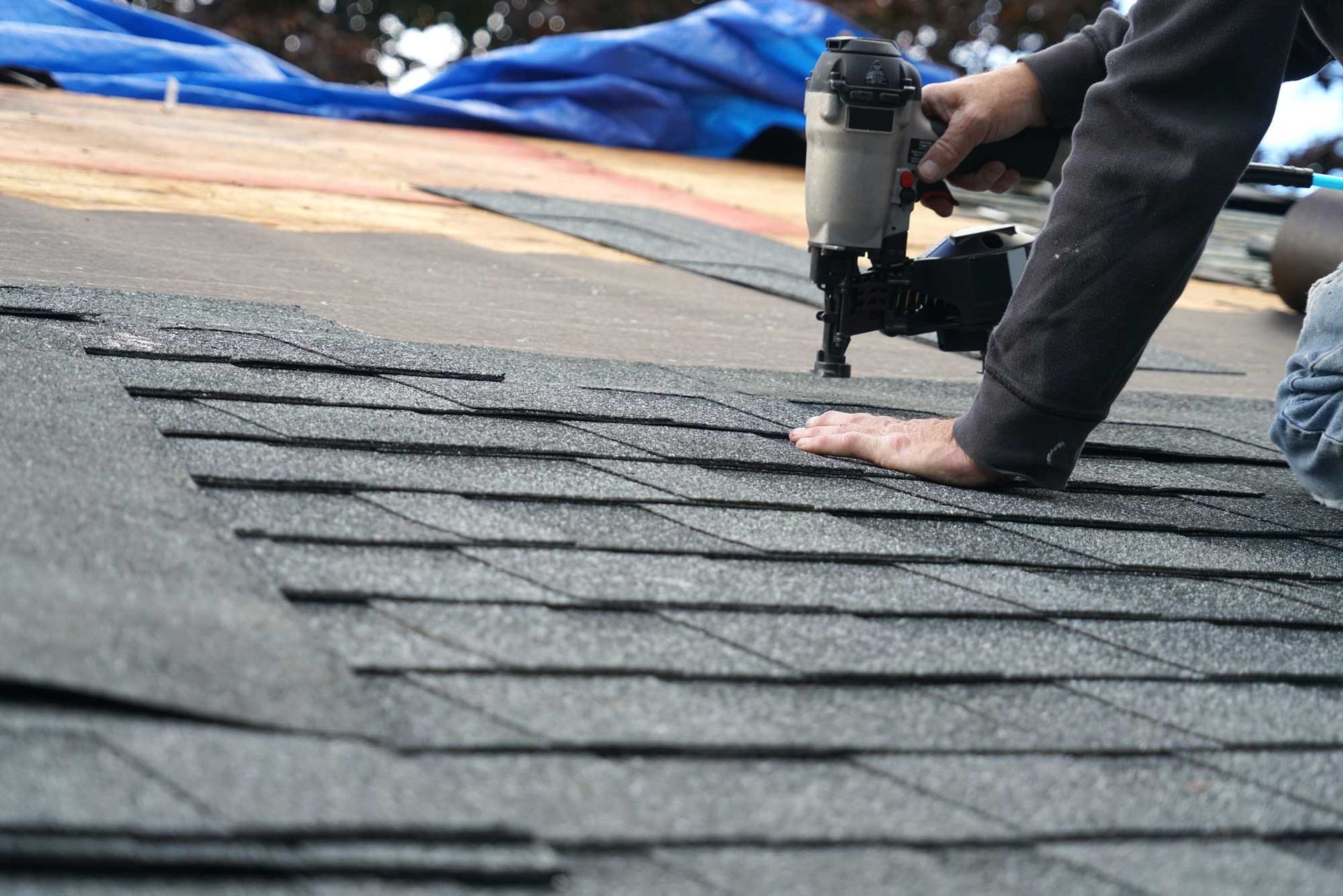 Roofer installing asphalt shingles with a nail gun on a roof surface. Roofer installing asphalt shingles with a nail gun on a roof surface.