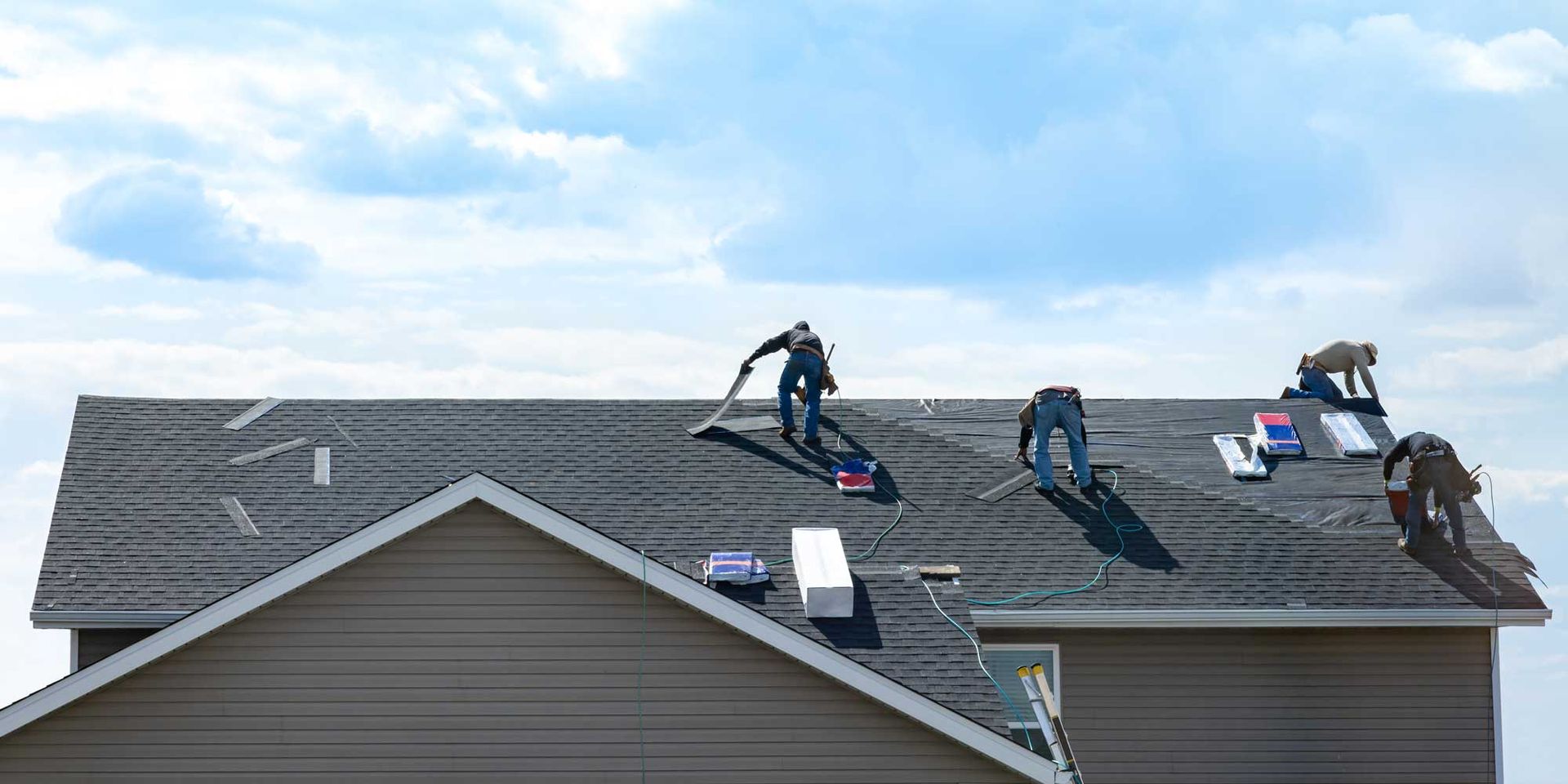 A roofing crew is installing new shingles on a residential home's roof using tools and materials