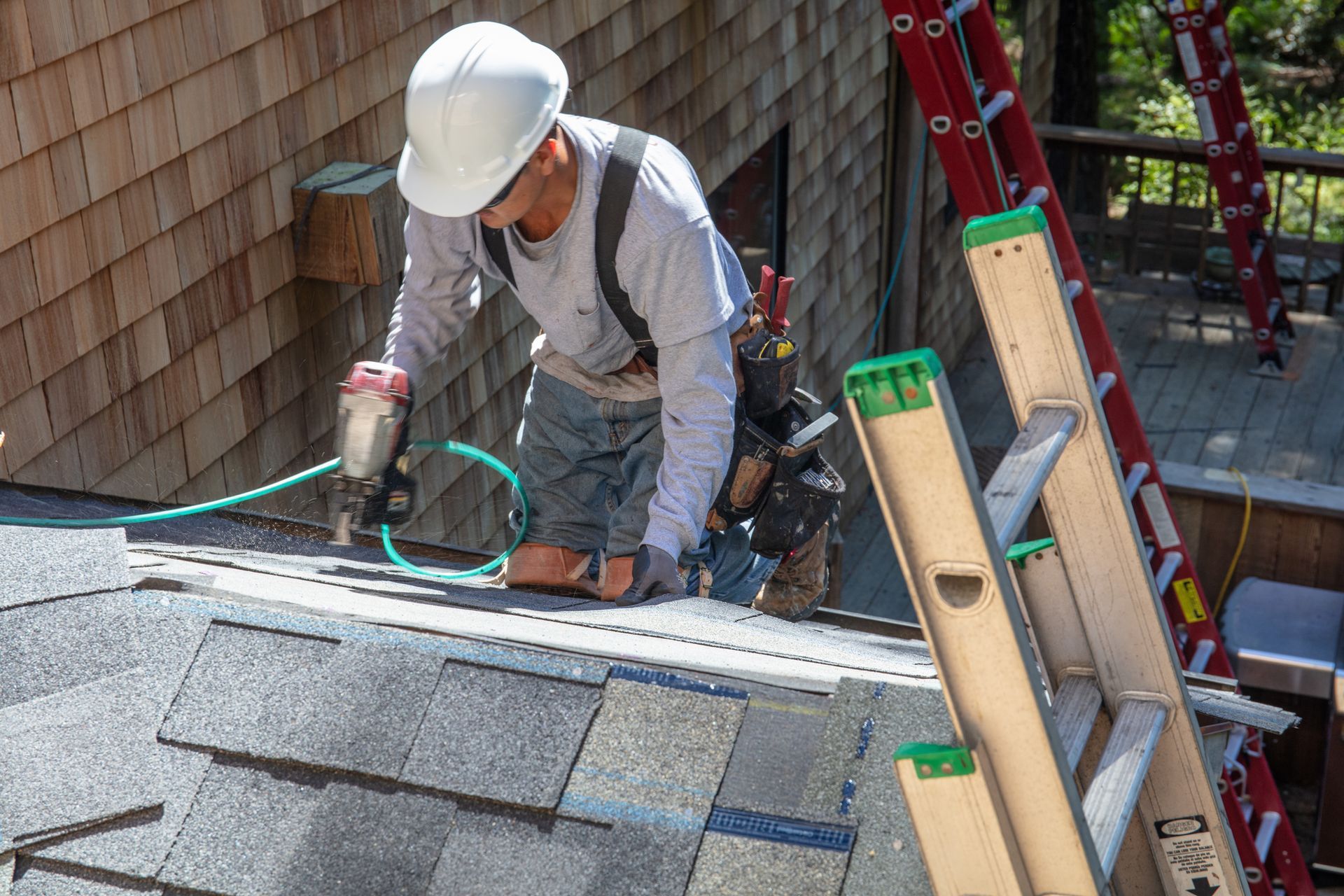 Residential roofing contractor installing asphalt shingles on home roof during construction work.