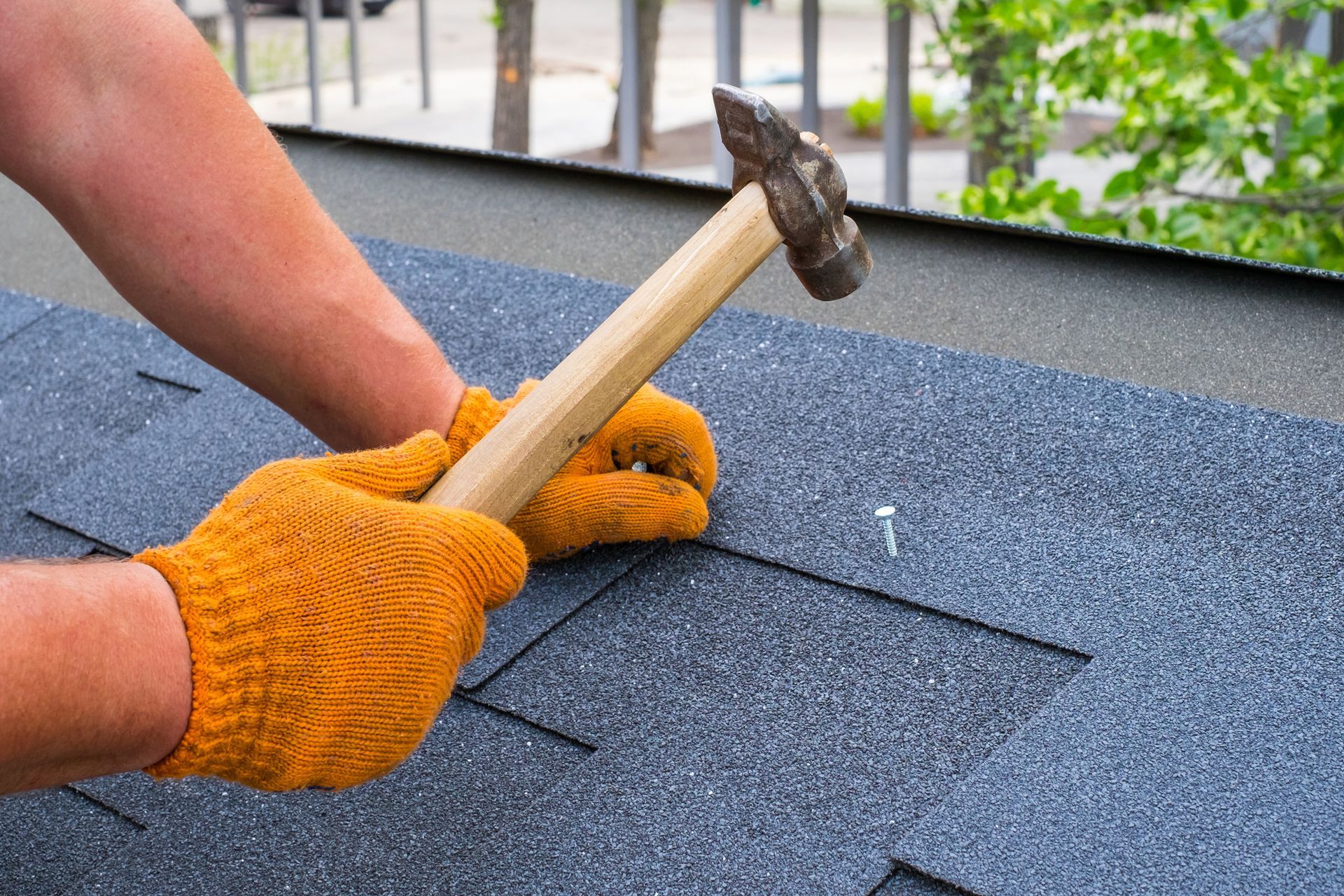 Roof repair company worker installing bitumen shingles with hammer tool