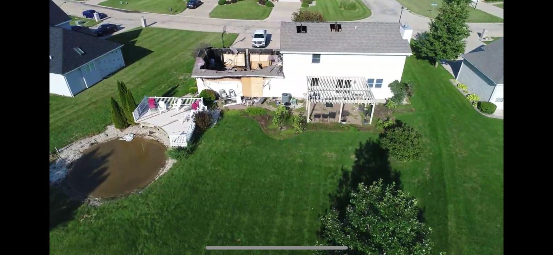Aerial view of a house with fire damage. Burnt roof and boarded windows are visible. Lush green lawn surrounds it.
