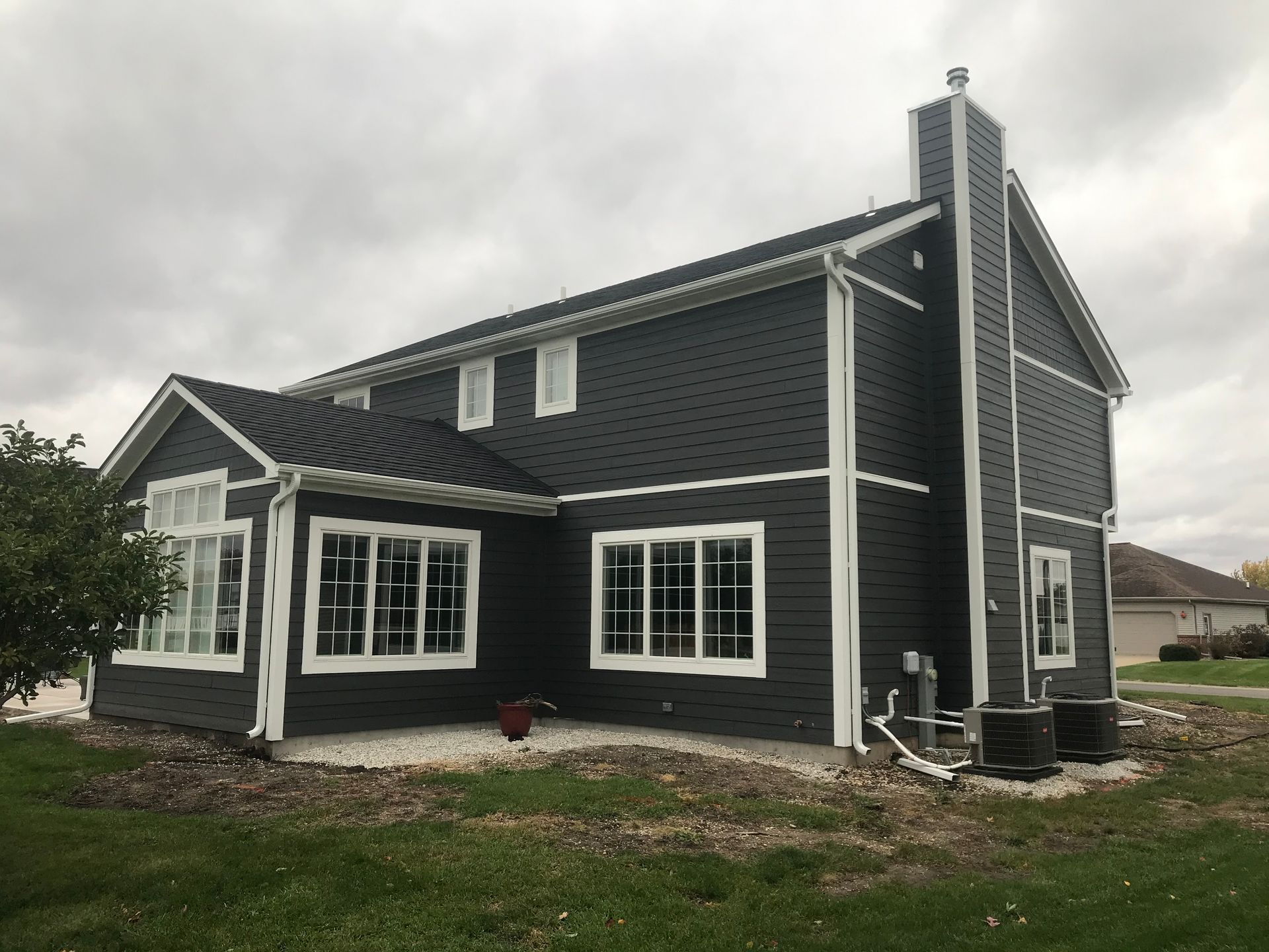 Dark gray house with white trim, windows, and chimney, under a cloudy sky.