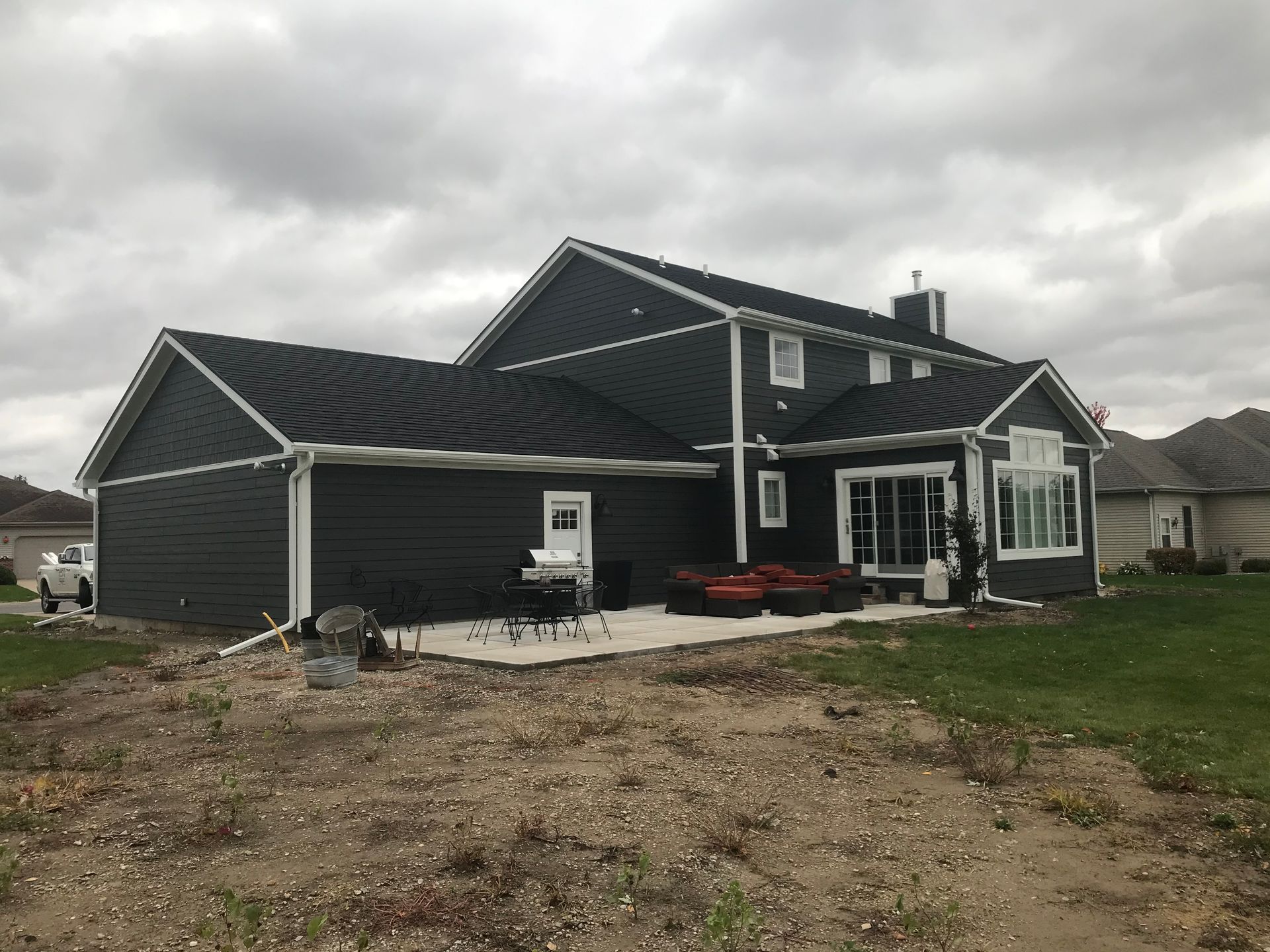 Dark gray house with white trim, patio, and cloudy sky.
