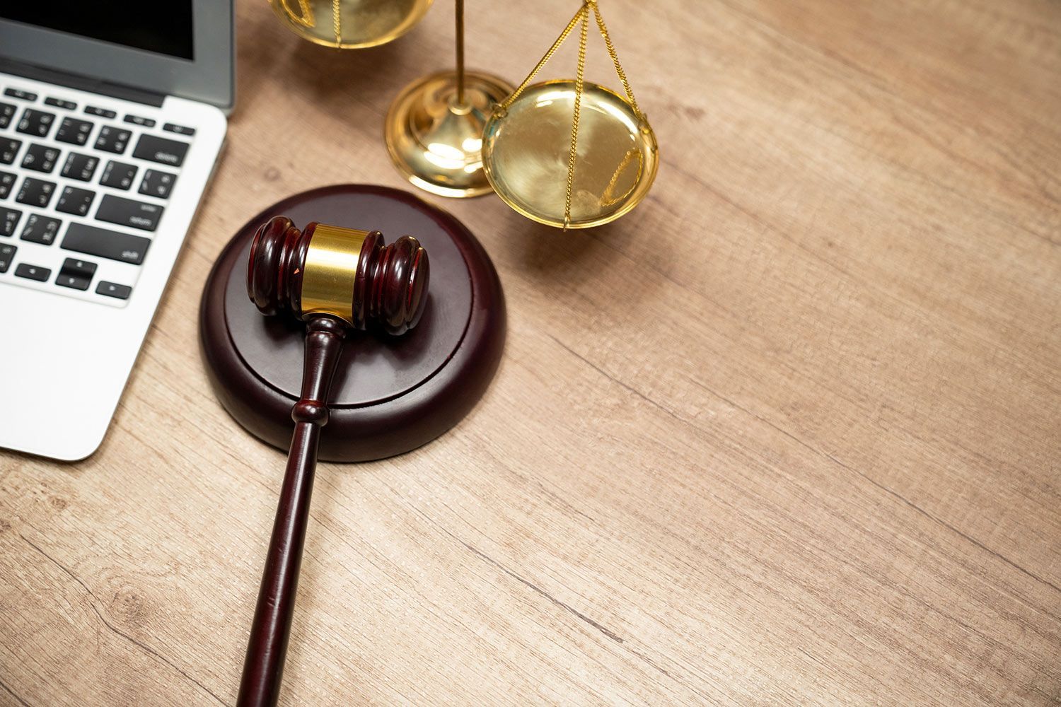 Laptop, gavel, and scales of justice on a wooden desk