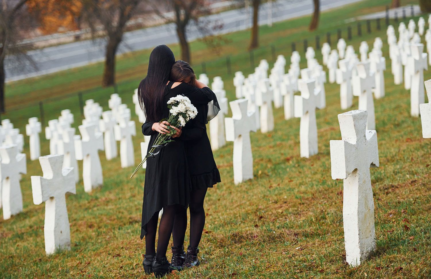 Two people embrace, and holding flowers in a cemetery