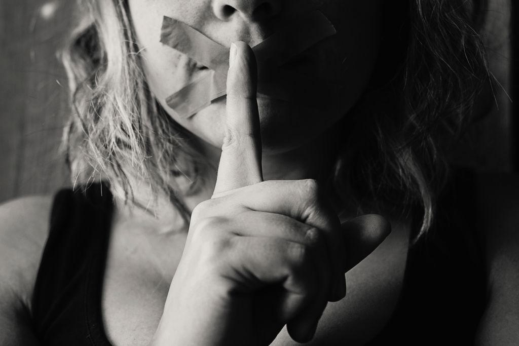 Woman with tape over mouth and suggesting silence