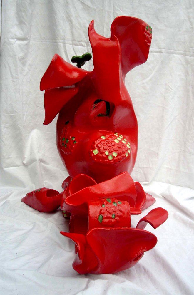 Abstrakte Plastik aus Pappmasché der Künstlerin Benita von Wendt. Titel: Daisy. Die abstrakte Skulptur ist rot mit hellgrünen Mosaiksteinen, anstatt eines Kopfes kommt aus ihrer Mitte heraus eine Blume. Die Plastik erinnert etwas an Daisy Duck, sie zieht eine Schleppe hinter sich her und hat übergroße Pömps an. Rückansicht.