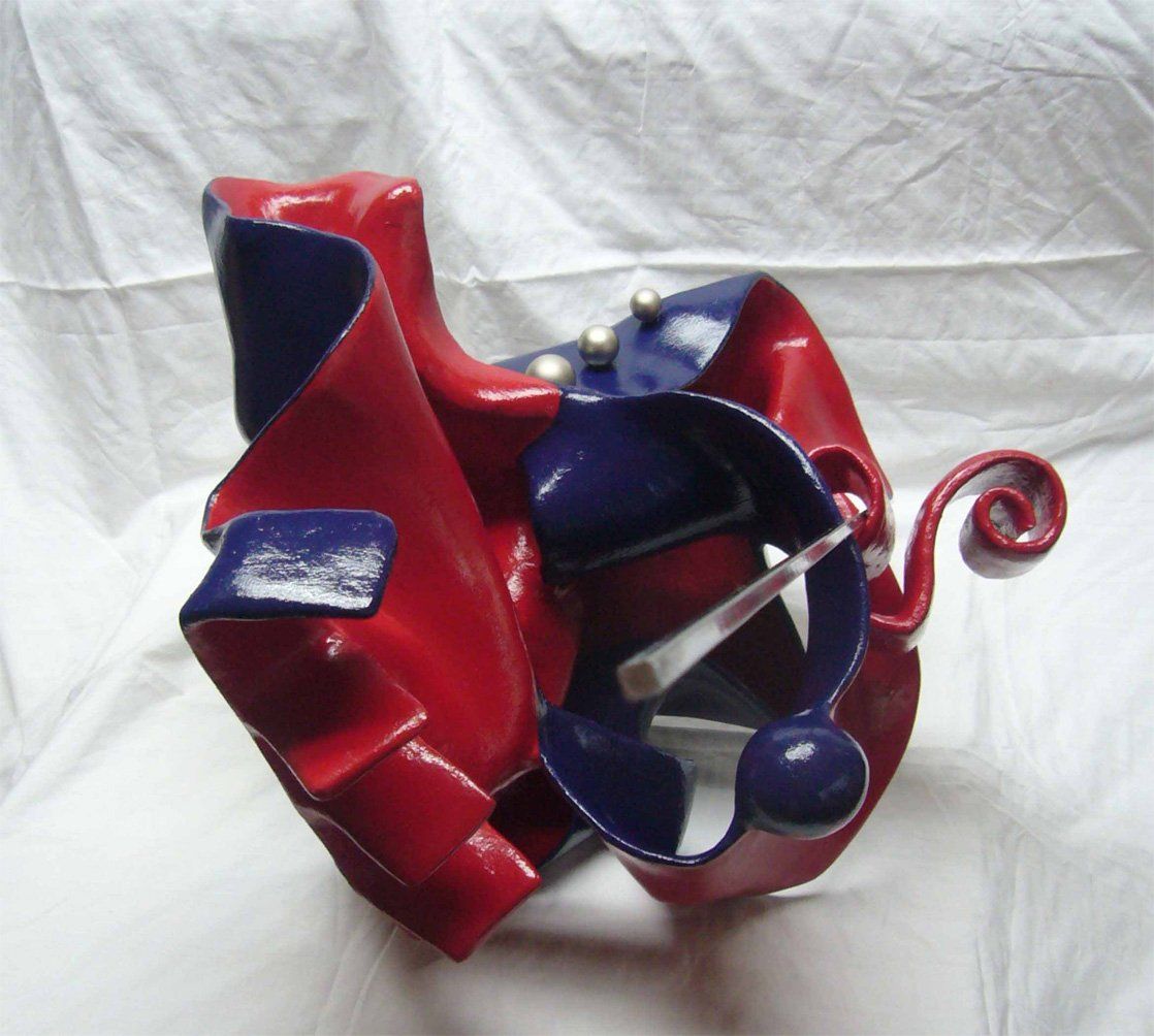 Abstrakte Plastik aus Pappmasché der Künstlerin Benita von Wendt. Titel: Don Quichotte. Die abstrakte Skulptur ist aussen Blau, innen rot, rechts sind Metallknöpfe befestigt, eine dünne Metallstange an der Skulptur erinnert an eine Lanze. Seitenansicht.