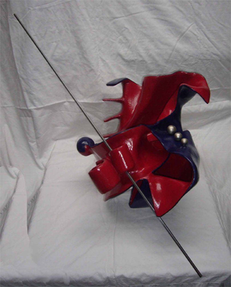 Abstrakte Plastik aus Pappmasché der Künstlerin Benita von Wendt. Titel: Don Quichotte. Die abstrakte Skulptur ist aussen Blau, innen rot, rechts sind Metallknöpfe befestigt, eine dünne Metallstange an der Skulptur erinnert an eine Lanze. Ansicht seitlich von oben.