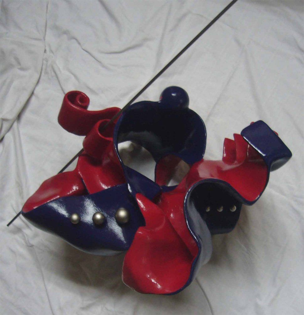 Abstrakte Plastik aus Pappmasché der Künstlerin Benita von Wendt. Titel: Don Quichotte. Die abstrakte Skulptur ist aussen Blau, innen rot, rechts sind Metallknöpfe befestigt, eine dünne Metallstange an der Skulptur erinnert an eine Lanze. Ansicht von oben.