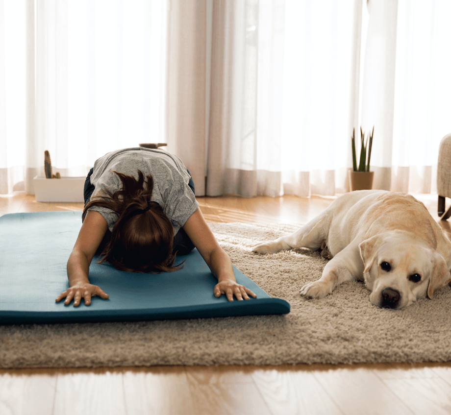 A woman is doing yoga on a yoga mat next to a dog.
