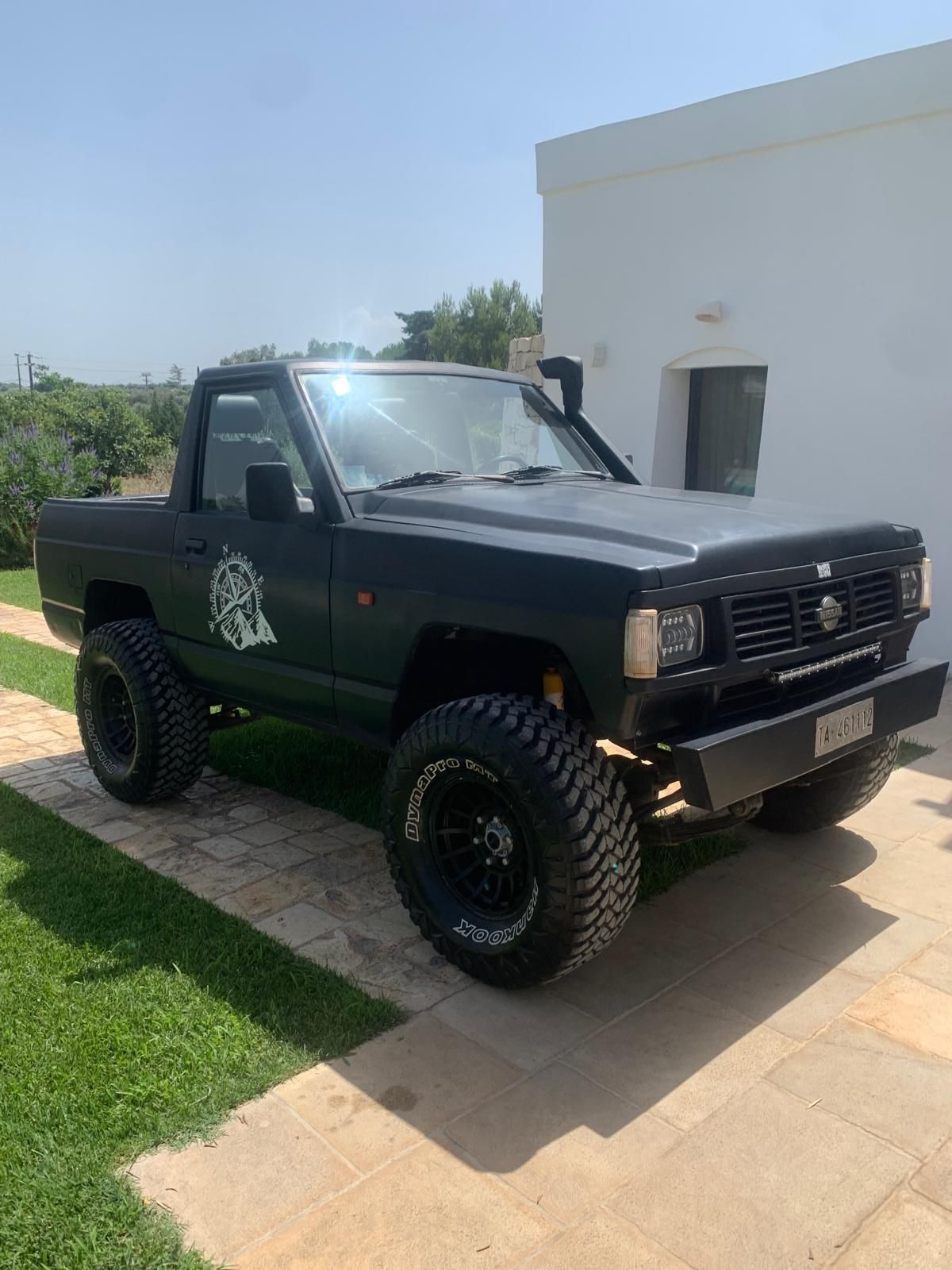 Un pick-up Nissan nero rialzato parcheggiato su un prato verde. Sullo sfondo un edificio.