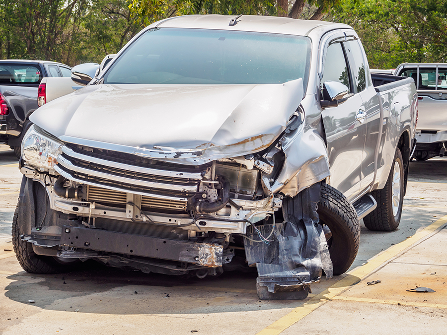 A silver truck with a damaged front end is parked in a parking lot.