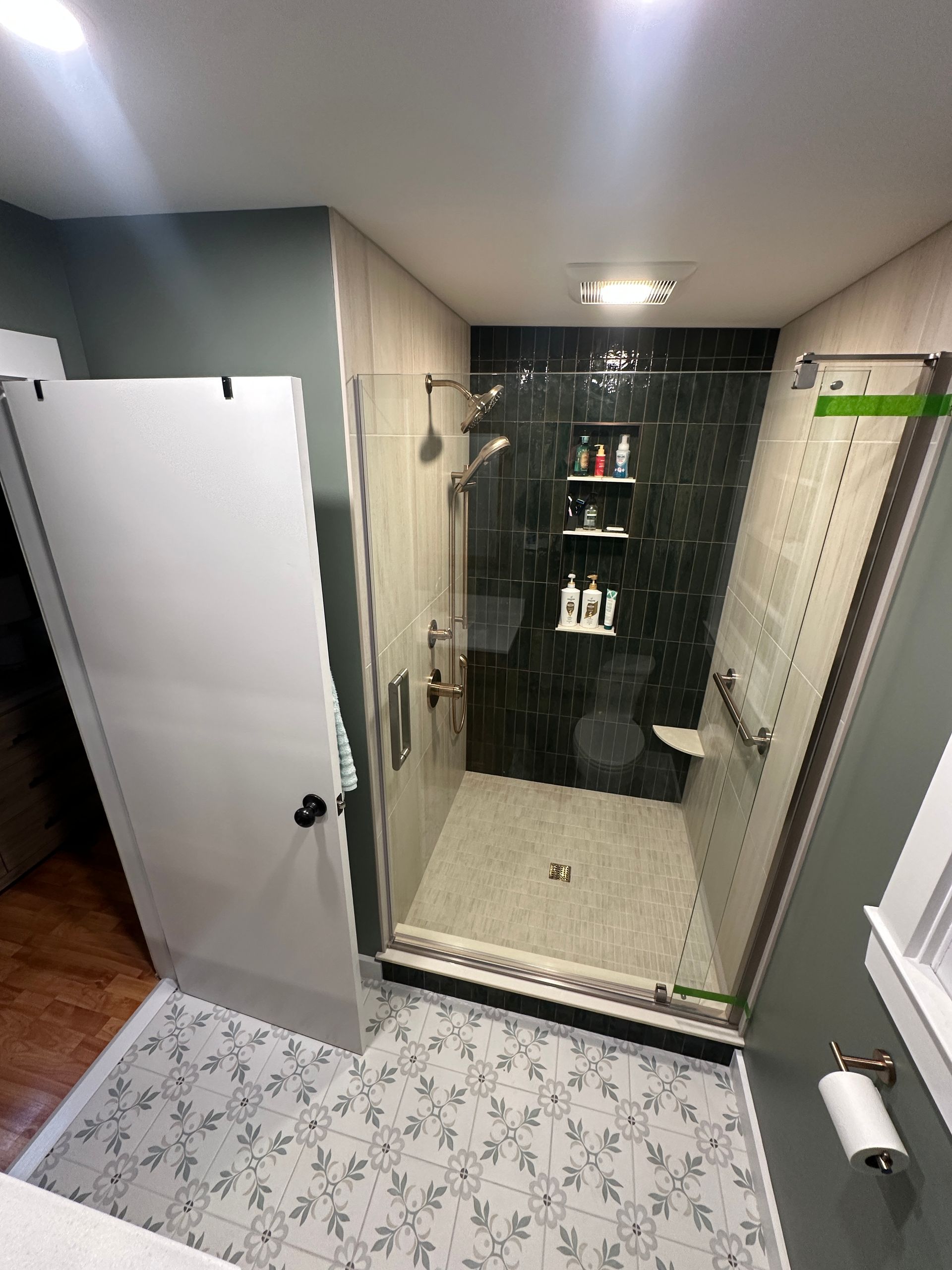 Modern shower with glass door, black tiled accent wall, and patterned floor.
