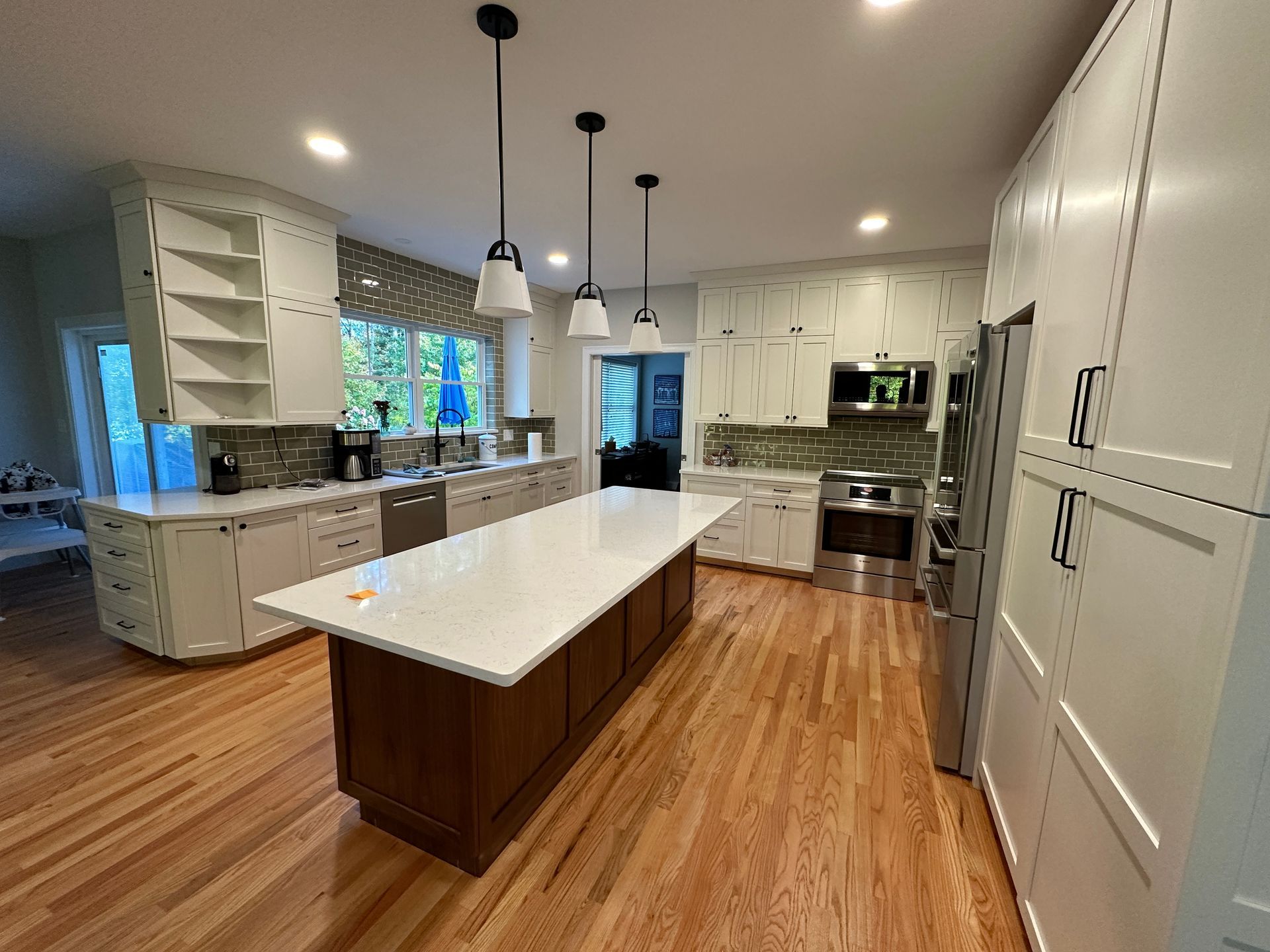 A kitchen with white cabinets , stainless steel appliances , hardwood floors and a large island.