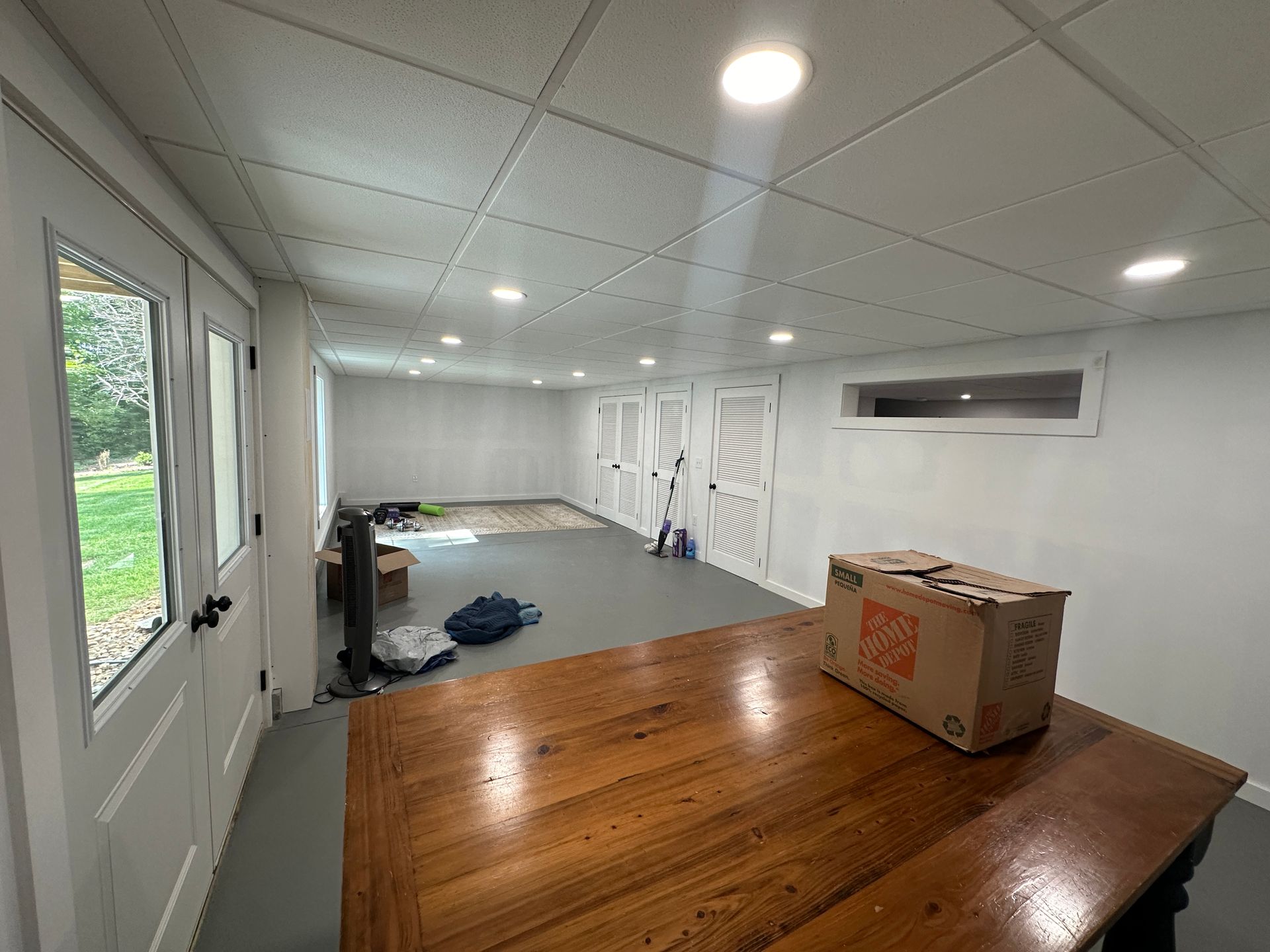 Empty, unfinished room with a wooden table, several doors, and ceiling lights.