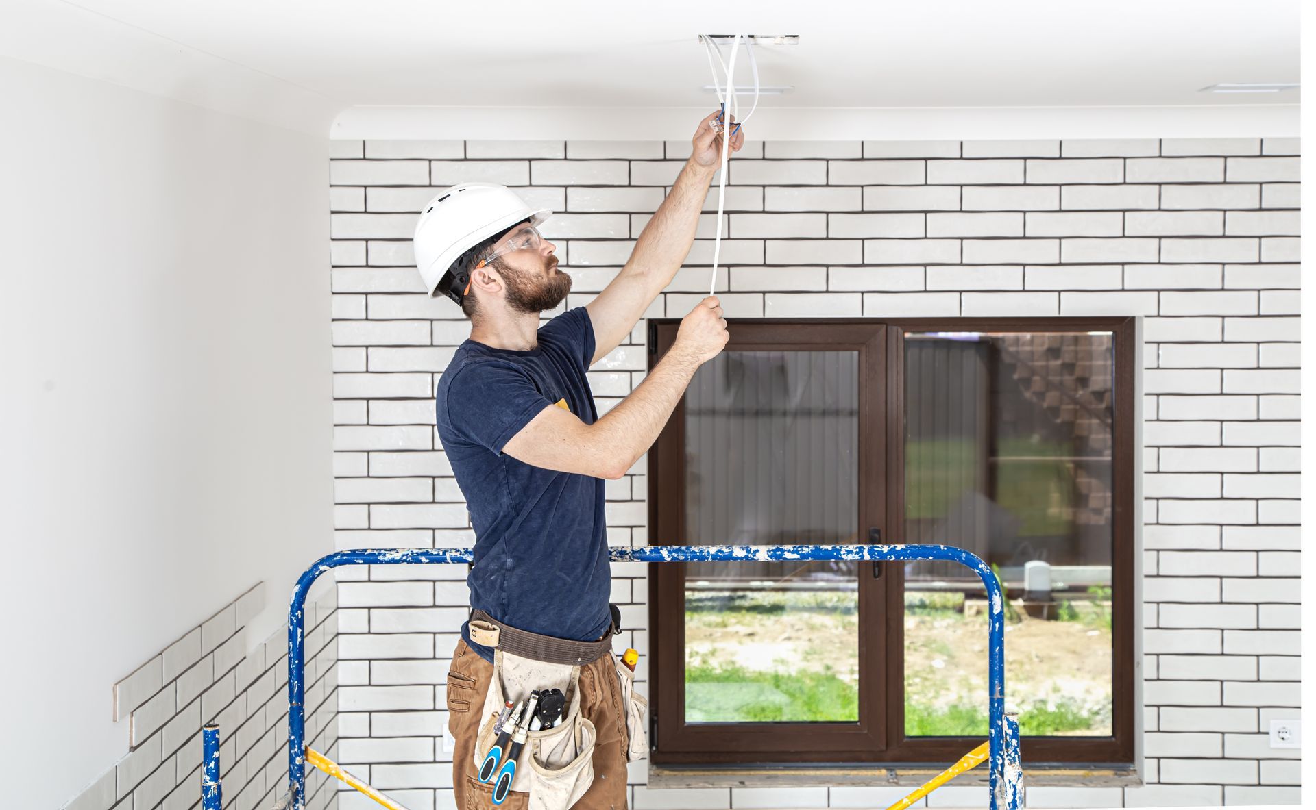 A man is measuring a ceiling with a tape measure while standing on a ladder.