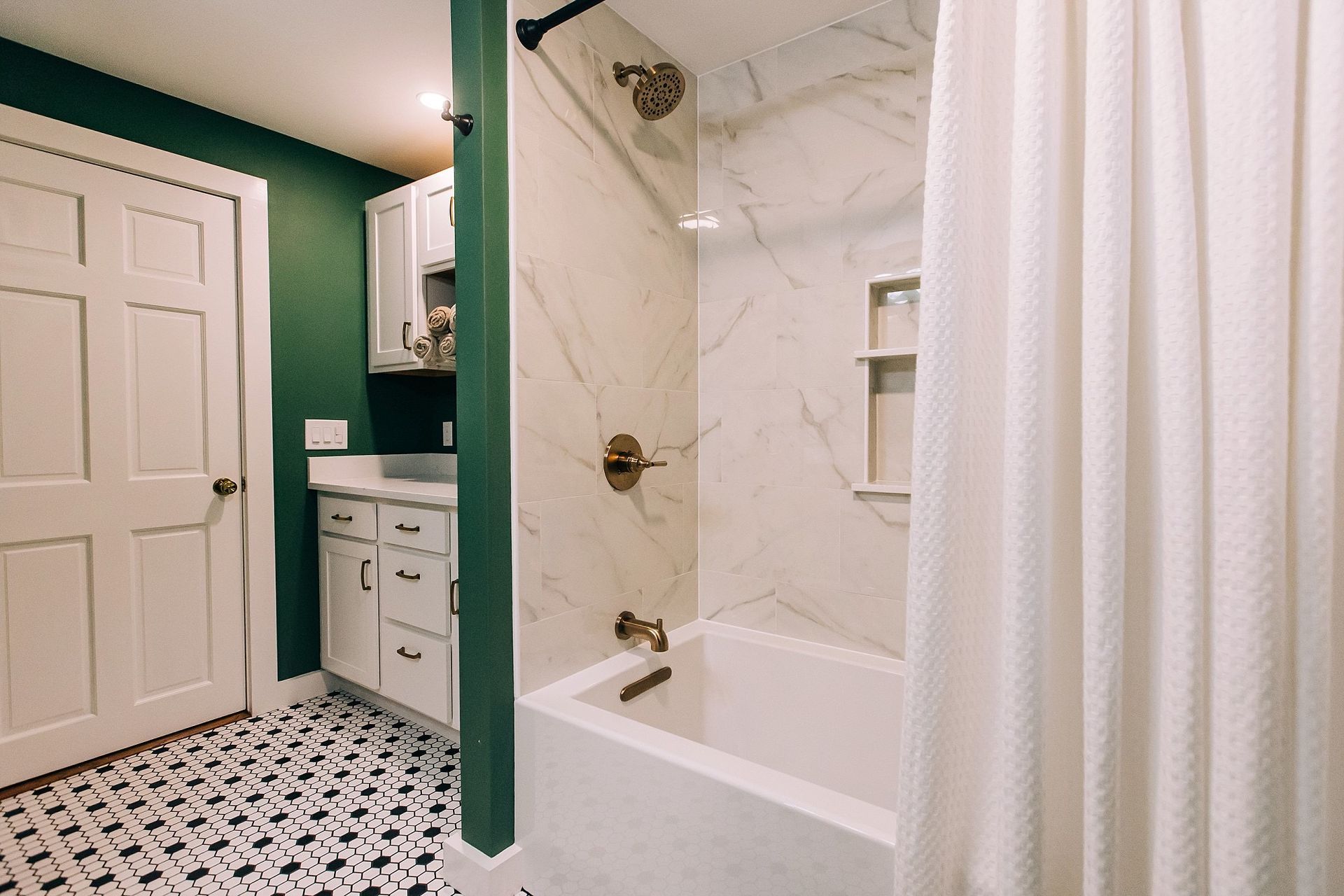 Bathroom with green wall, white door, black and white patterned floor, and white marble shower.