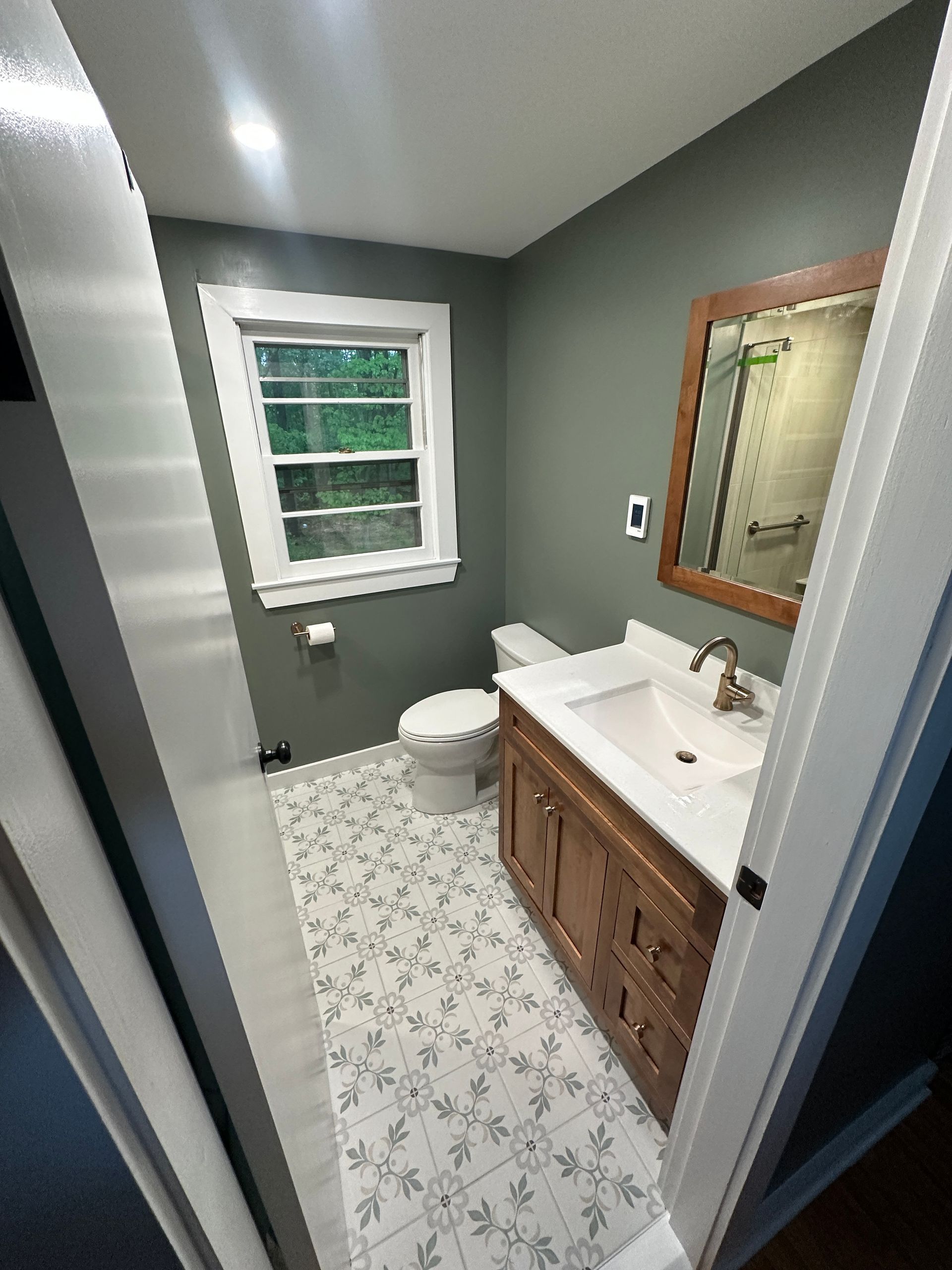 A bathroom with a toilet , sink , mirror and window.